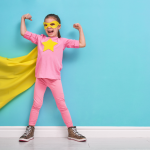 A girl dressed as a superhero. holding arms up to signify she is strong and happy